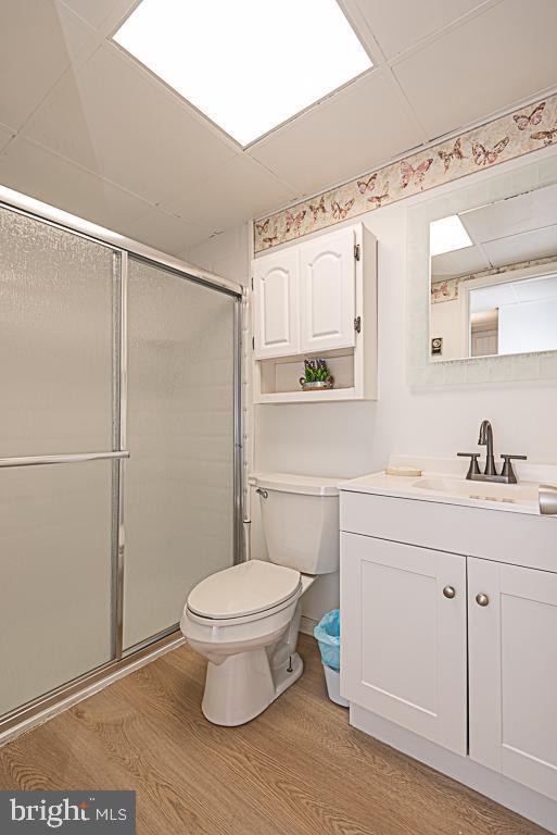 bathroom featuring vanity, hardwood / wood-style flooring, a shower with shower door, and toilet