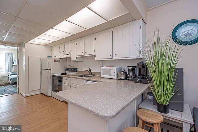 kitchen with white cabinetry, white appliances, kitchen peninsula, and sink