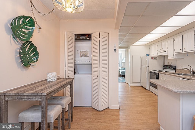 kitchen with stacked washer / drying machine, sink, light wood-type flooring, white appliances, and white cabinets