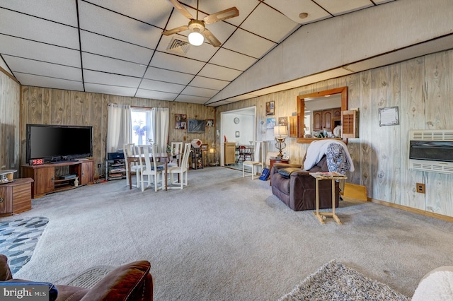 living room with vaulted ceiling, heating unit, wooden walls, carpet floors, and ceiling fan