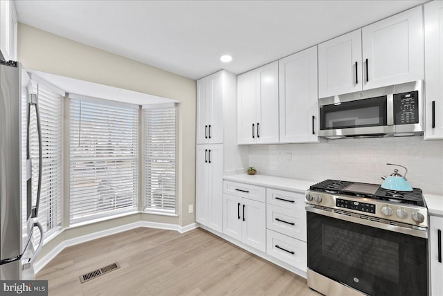 kitchen featuring backsplash, light wood-type flooring, white cabinets, and appliances with stainless steel finishes