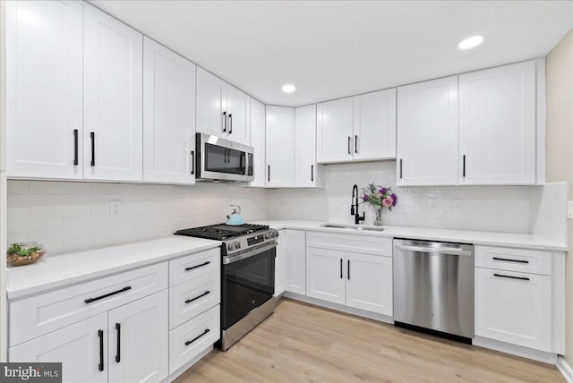 kitchen featuring sink, stainless steel appliances, white cabinets, decorative backsplash, and light wood-type flooring