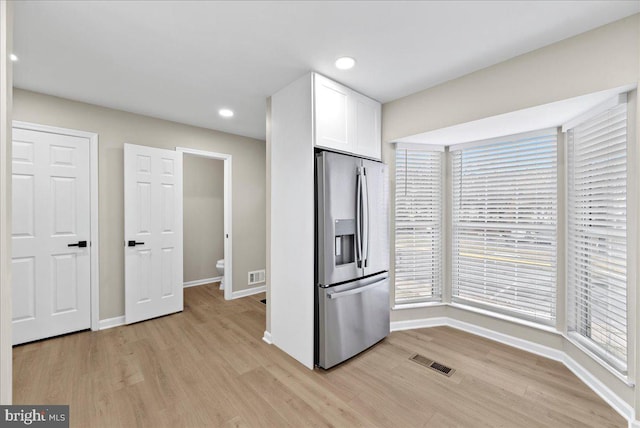 kitchen featuring stainless steel fridge, light wood-type flooring, and white cabinets