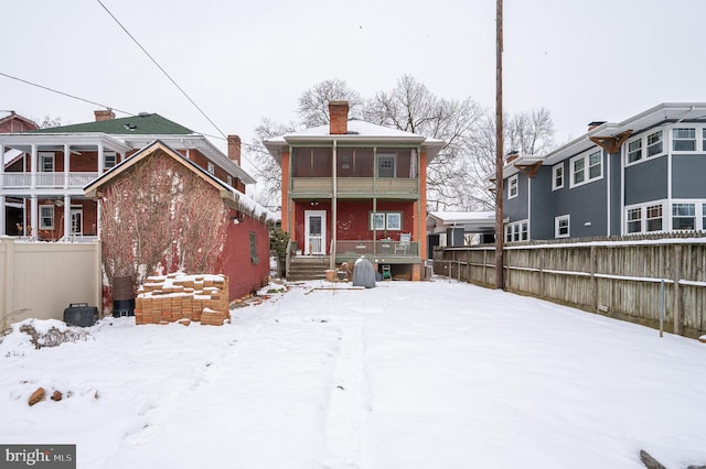 snow covered back of property featuring a sunroom