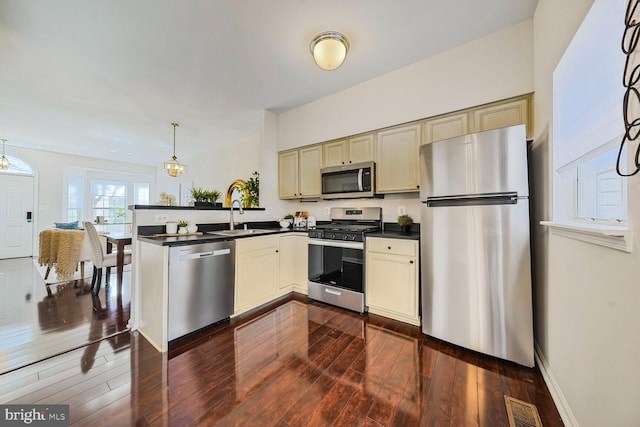 kitchen with a sink, dark countertops, appliances with stainless steel finishes, and cream cabinets