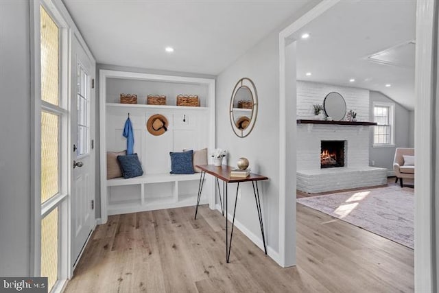 mudroom featuring built in features, lofted ceiling, a fireplace, and light wood-type flooring