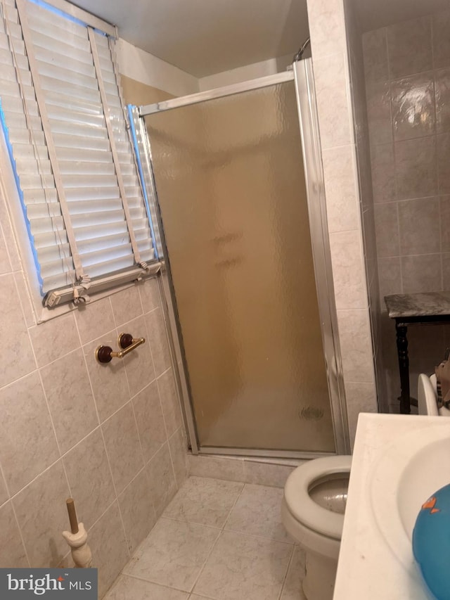 bathroom with toilet, a shower with door, and tile walls