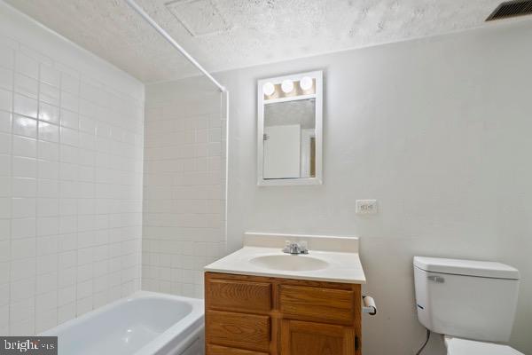 full bathroom featuring tiled shower / bath combo, vanity, a textured ceiling, and toilet