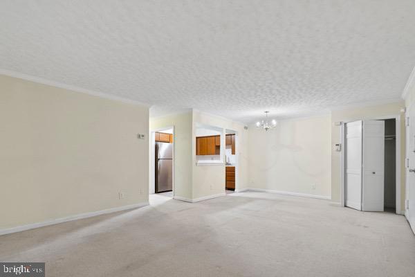 empty room with ornamental molding, light colored carpet, a chandelier, and a textured ceiling