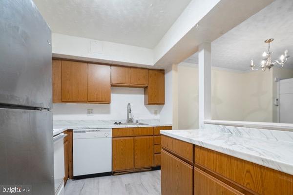 kitchen featuring sink, light hardwood / wood-style flooring, stainless steel refrigerator, dishwasher, and pendant lighting