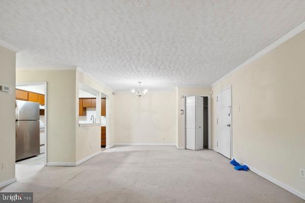 carpeted spare room with crown molding, an inviting chandelier, and a textured ceiling