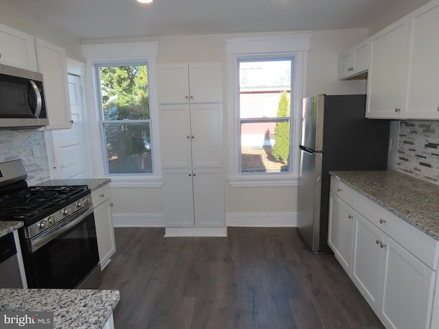 kitchen with appliances with stainless steel finishes, backsplash, white cabinets, and light stone counters