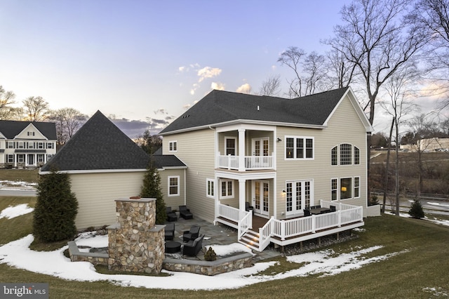 snow covered house with a lawn, french doors, a deck, and a balcony