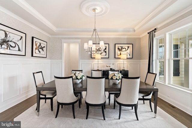 dining area featuring a notable chandelier, crown molding, wood-type flooring, and a tray ceiling