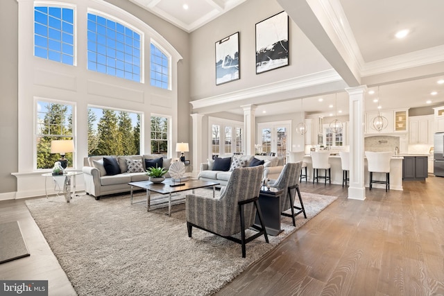 living room with light wood-type flooring, ornate columns, beamed ceiling, and ornamental molding