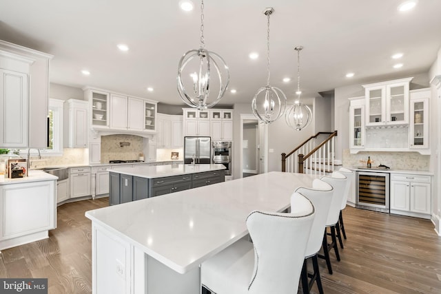 kitchen featuring a kitchen bar, beverage cooler, white cabinetry, decorative light fixtures, and a large island