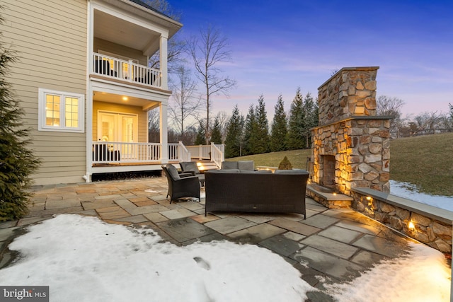 patio terrace at dusk featuring a balcony and an outdoor living space with a fireplace