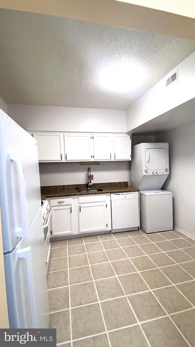 clothes washing area featuring stacked washer / dryer, light tile patterned flooring, sink, and a textured ceiling