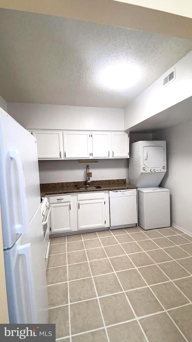 washroom featuring sink, light tile patterned floors, a textured ceiling, and stacked washing maching and dryer