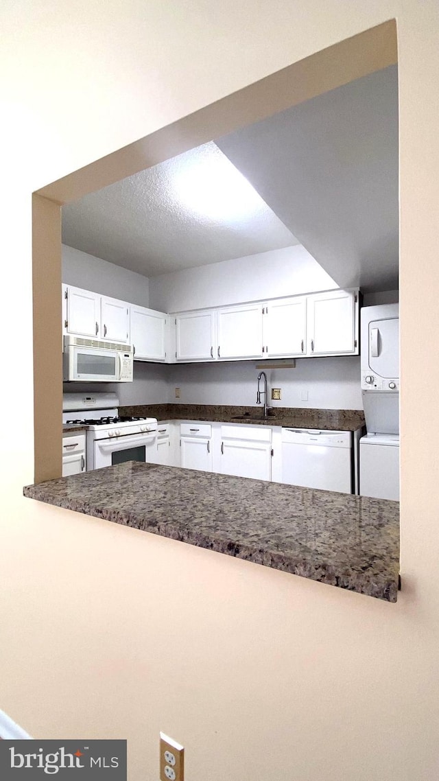 kitchen with white cabinetry, stacked washer / drying machine, sink, and white appliances