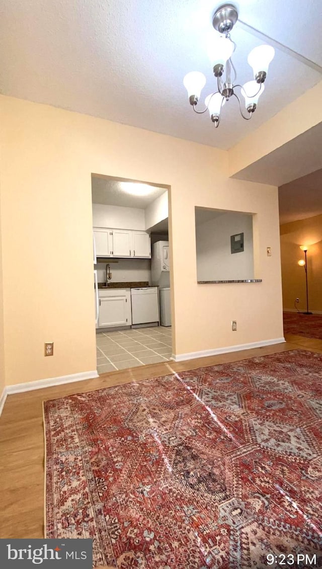 unfurnished living room with sink, a textured ceiling, a notable chandelier, and light wood-type flooring