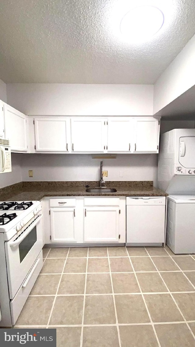 kitchen featuring light tile patterned floors, stacked washer and dryer, white appliances, sink, and white cabinets