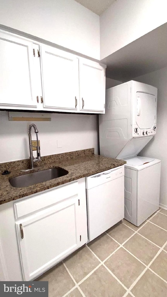 washroom with light tile patterned flooring, stacked washer and dryer, sink, and cabinets