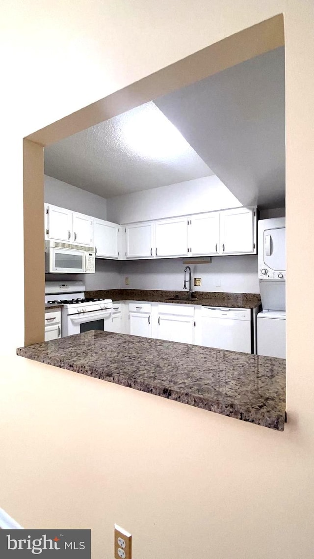 kitchen featuring white appliances, stacked washer / dryer, sink, and white cabinets