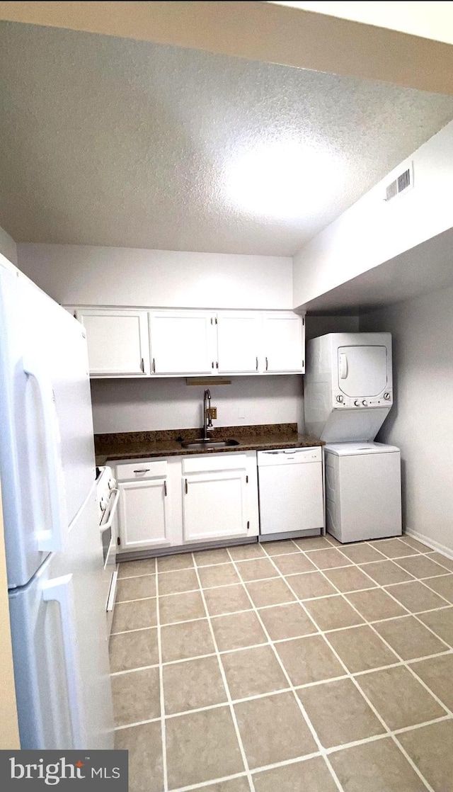 laundry area with sink, light tile patterned flooring, a textured ceiling, and stacked washer / dryer