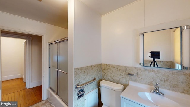 full bathroom with enclosed tub / shower combo, tile walls, vanity, wood-type flooring, and toilet