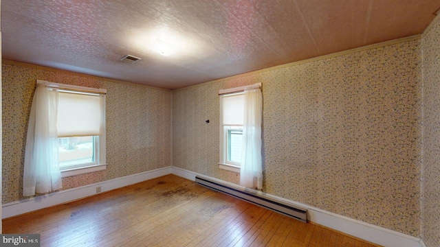 spare room with hardwood / wood-style flooring, a baseboard heating unit, a wealth of natural light, and a textured ceiling