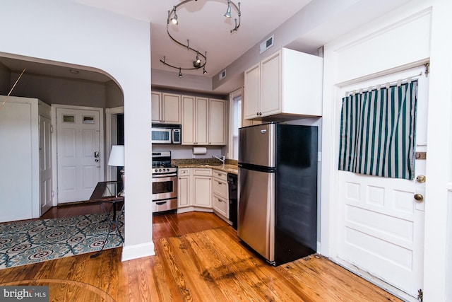 kitchen with white cabinetry, stainless steel appliances, light hardwood / wood-style floors, and dark stone counters