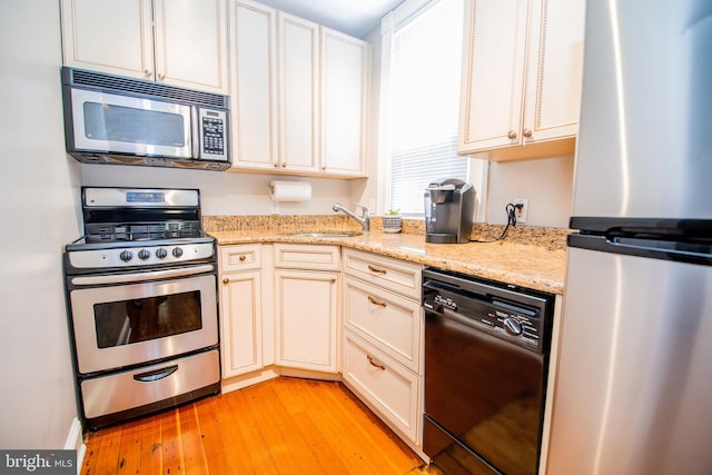 kitchen featuring stainless steel appliances, light stone countertops, sink, and light hardwood / wood-style flooring