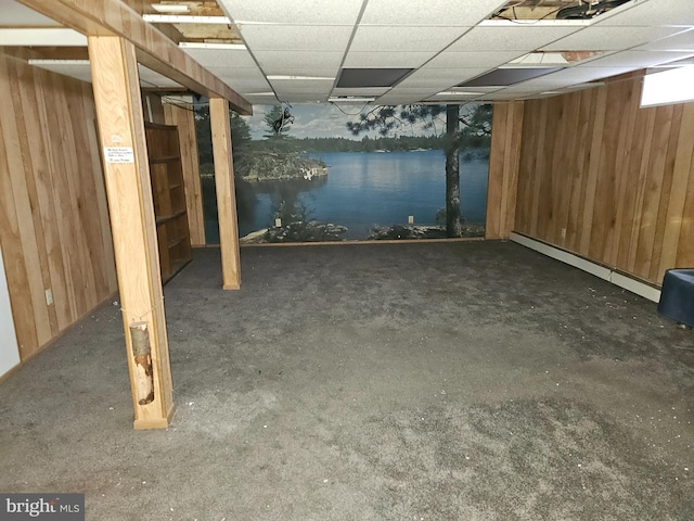 basement featuring a baseboard heating unit, a drop ceiling, and wood walls