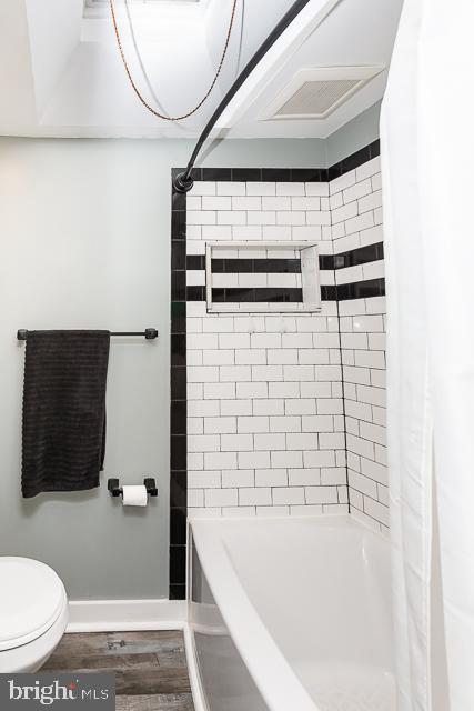 bathroom with wood-type flooring, toilet, and tiled shower / bath