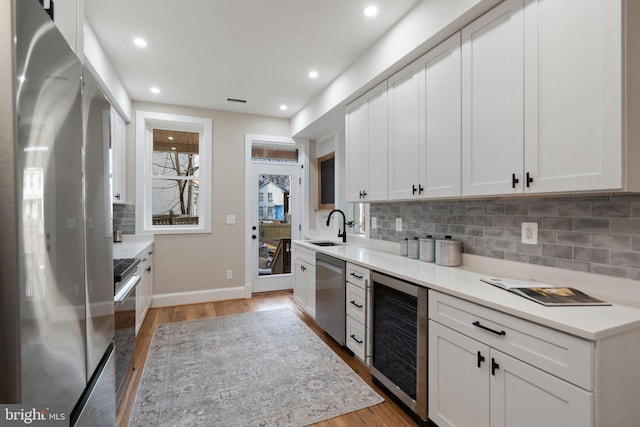 kitchen with wine cooler, stainless steel appliances, sink, and white cabinets