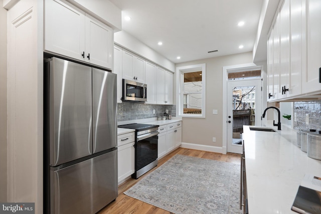 kitchen featuring sink, light wood-type flooring, white cabinets, stainless steel appliances, and backsplash