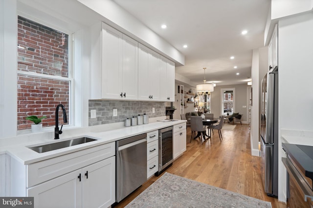 kitchen with sink, appliances with stainless steel finishes, hanging light fixtures, white cabinets, and beverage cooler