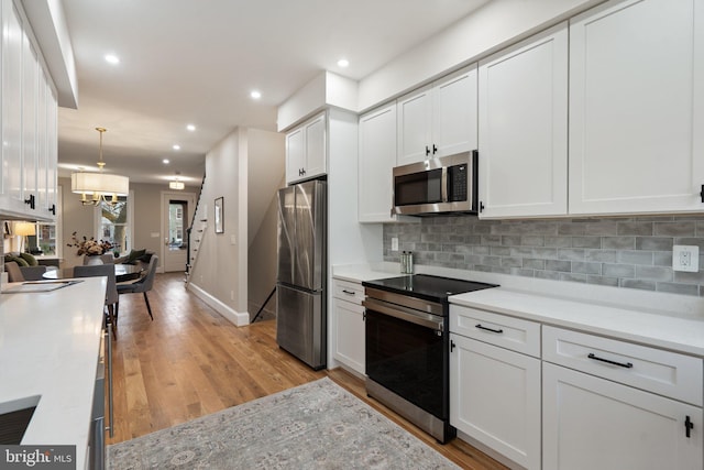 kitchen featuring decorative light fixtures, tasteful backsplash, white cabinetry, stainless steel appliances, and light wood-type flooring