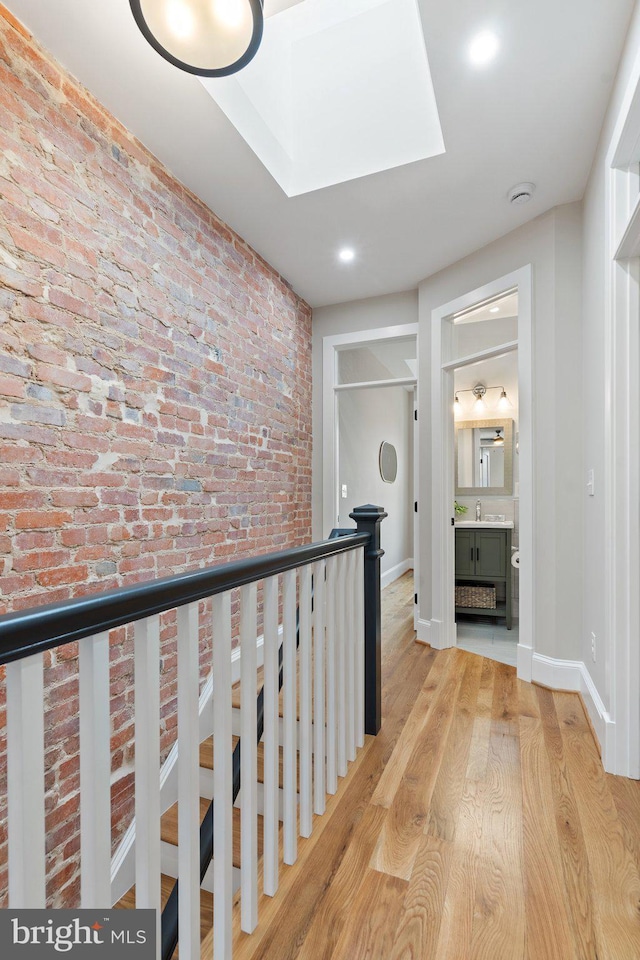 hallway featuring brick wall, a skylight, sink, and light hardwood / wood-style flooring