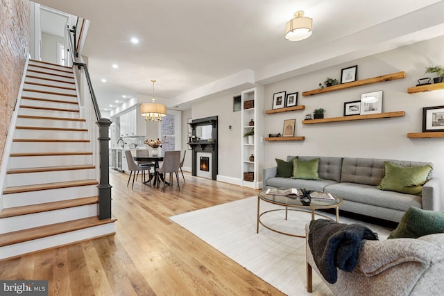 living room with built in shelves, recessed lighting, light wood-style floors, stairs, and an inviting chandelier