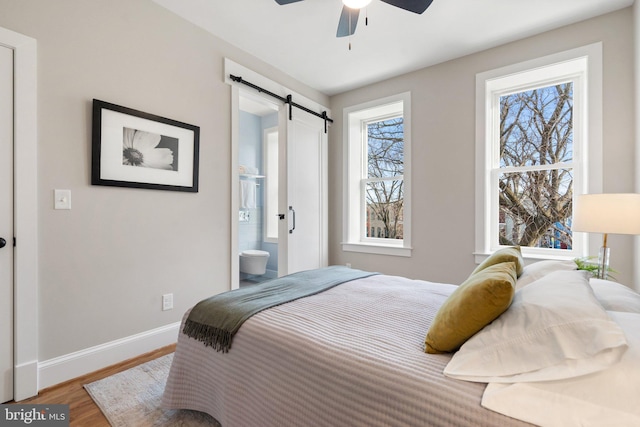 bedroom with hardwood / wood-style floors, a barn door, ceiling fan, and ensuite bathroom