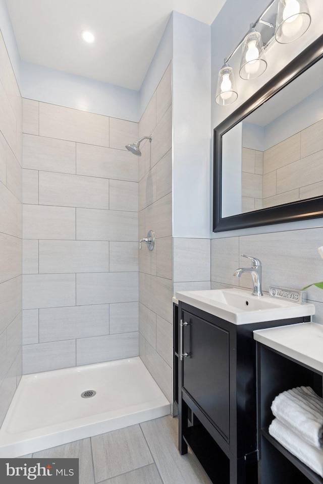 bathroom featuring vanity, a tile shower, backsplash, and tile walls