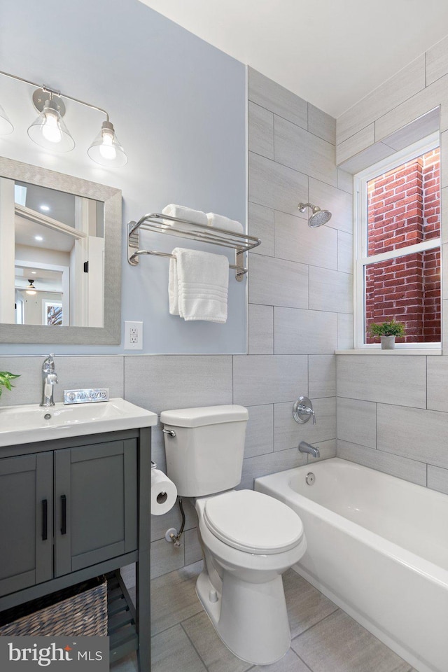 full bathroom with tile walls, vanity, tiled shower / bath combo, and toilet