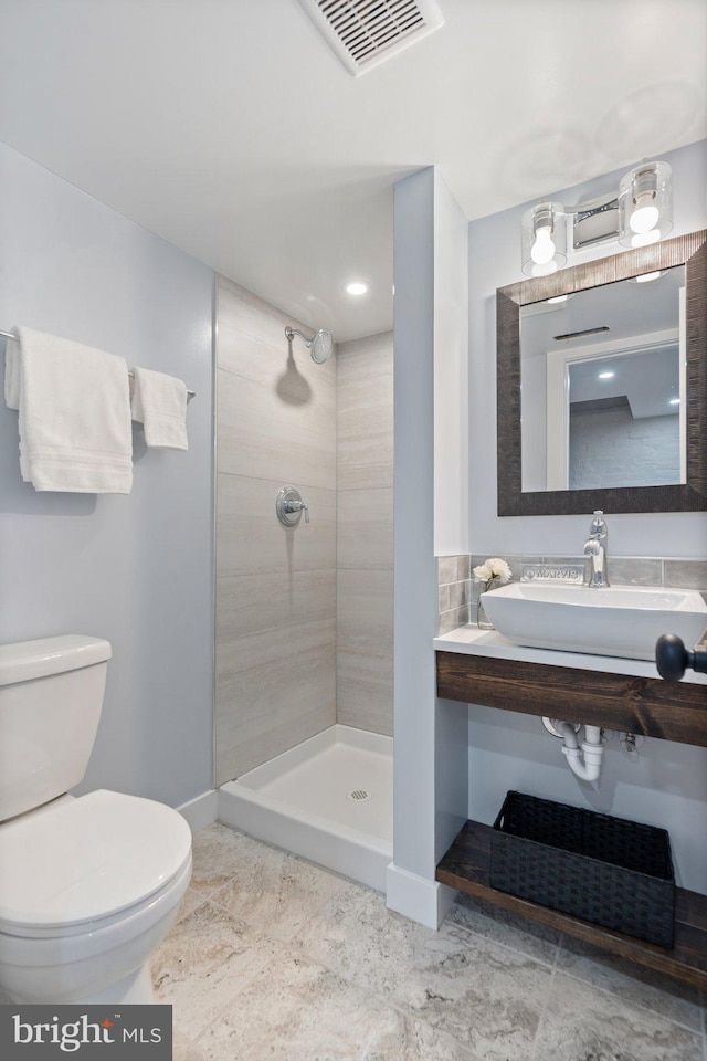 bathroom featuring sink, a tile shower, and toilet