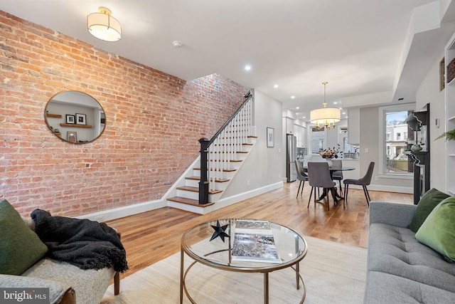 living room featuring brick wall, a notable chandelier, and light wood-type flooring