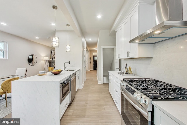 kitchen with sink, white cabinetry, decorative light fixtures, stainless steel appliances, and wall chimney range hood