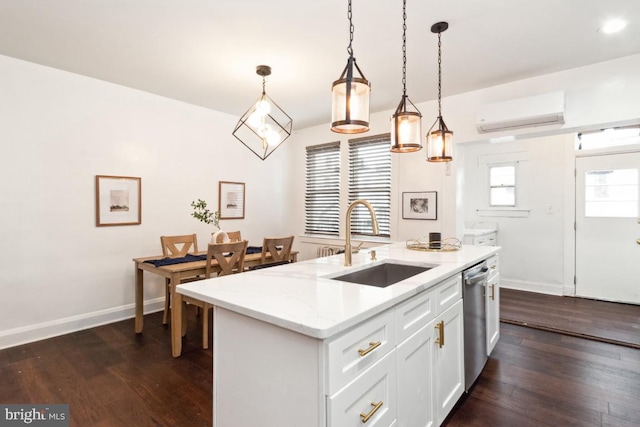 kitchen with decorative light fixtures, sink, white cabinets, a center island with sink, and a wall unit AC