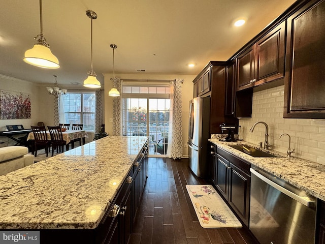 kitchen with sink, hanging light fixtures, a center island, stainless steel appliances, and light stone countertops