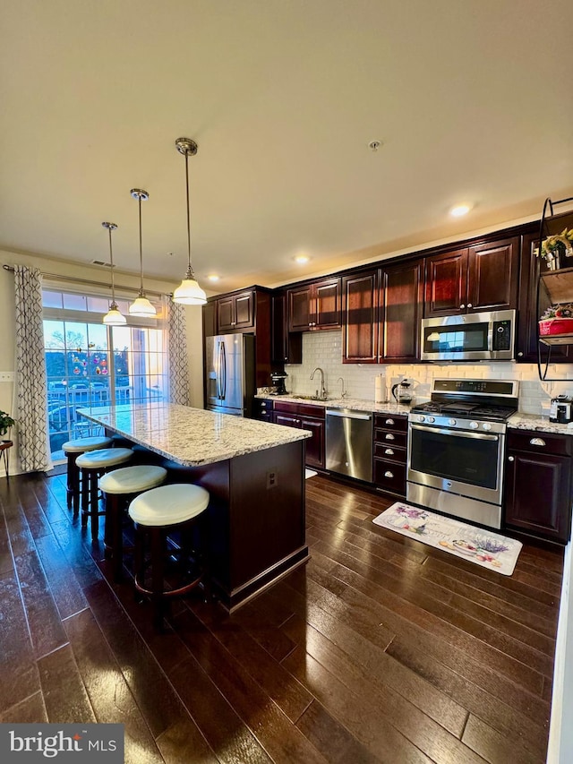 kitchen featuring a breakfast bar, a center island, appliances with stainless steel finishes, pendant lighting, and light stone countertops